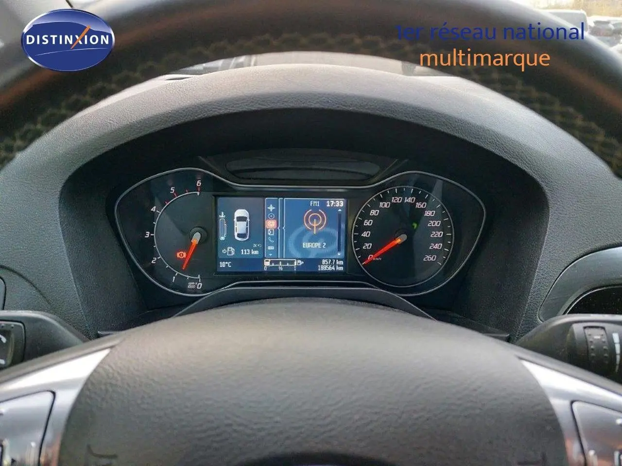 Tableau de bord et compteur numérique du Ford S-MAX gris clair, vue centrée depuis le volant.