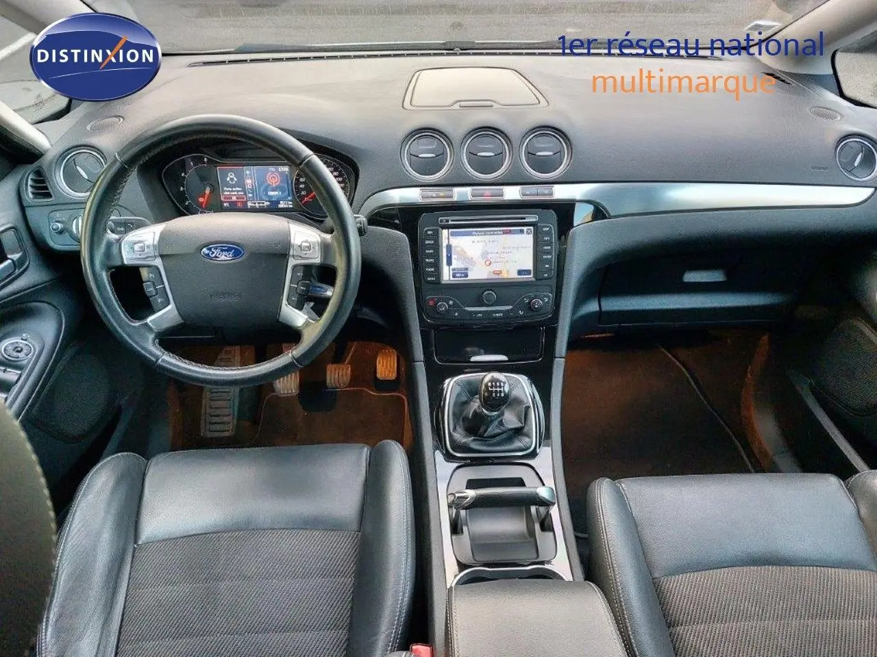 Vue intérieure du tableau de bord et console centrale du Ford S-MAX gris clair, avec volant multifonction et GPS intégré.