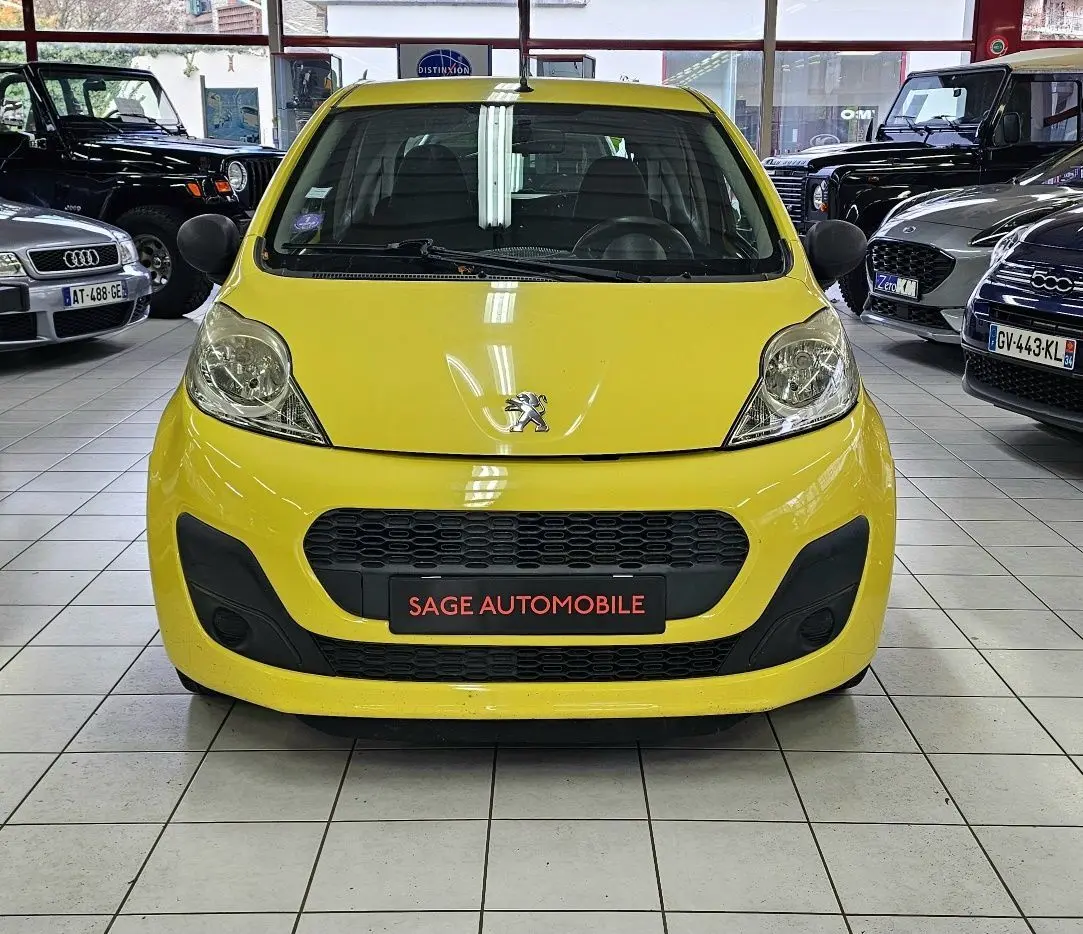Vue frontale d'une Peugeot 107 jaune vif exposée en showroom avec calandre noire et logo lion visible.