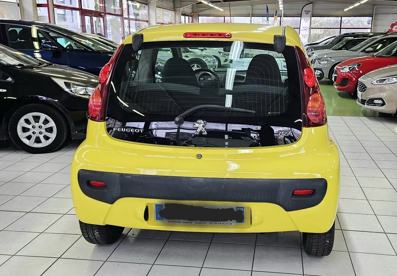 Vue arrière d'une Peugeot 107 jaune 2013 avec pare-chocs noir et feux arrière verticaux en concession.