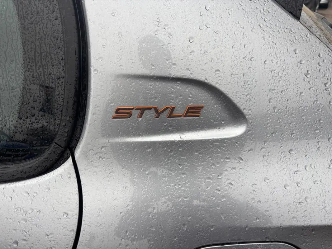 Gros plan sur l'aile arrière droite grise d'une Peugeot 208 Hybrid 100 e-DCS6 Style avec logo "STYLE" sous la pluie.