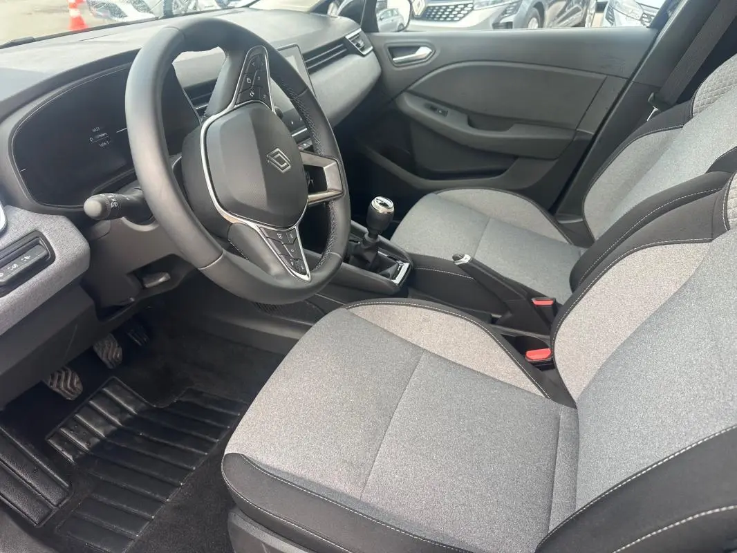 Vue intérieure côté conducteur de la Renault Clio V dCi 100 Evolution 2025, sièges gris, volant multifonction et boîte manuelle.