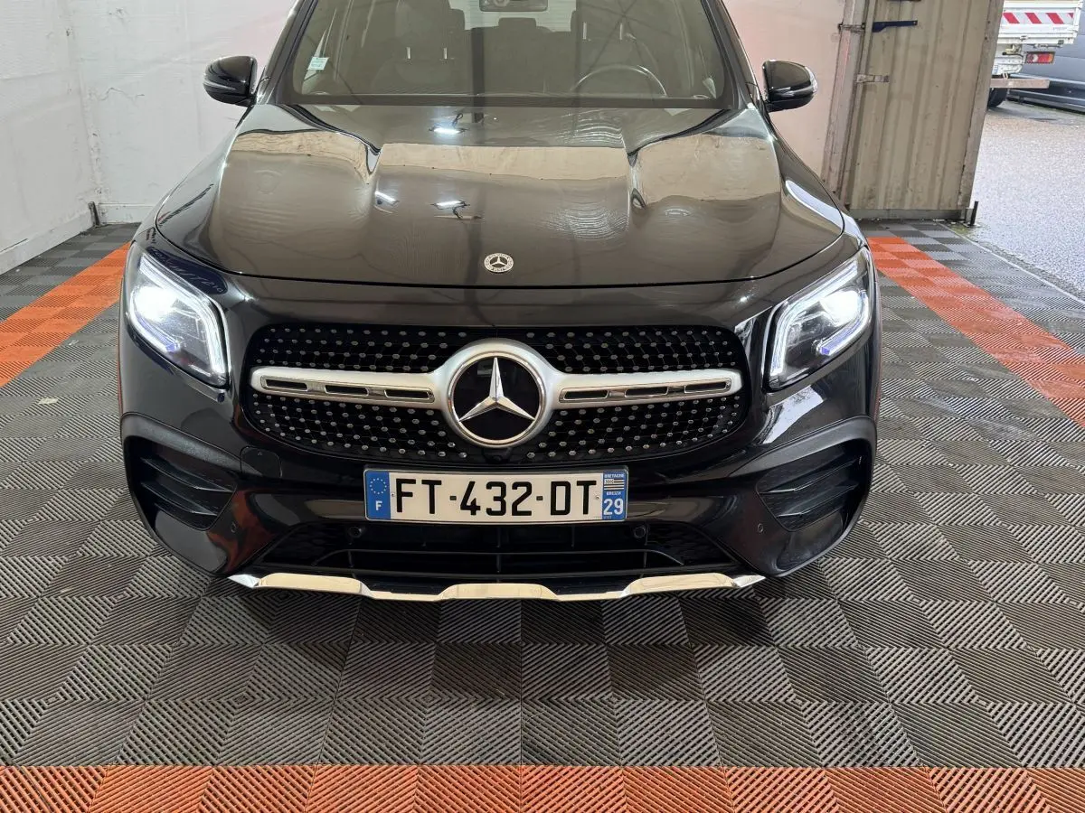 Vue de face du Mercedes GLB 200 d AMG Line noir avec calandre étoilée et phares LED allumés dans un garage.