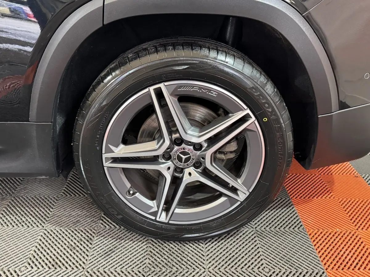 Gros plan sur la roue avant droite noire du Mercedes GLB 200 d AMG Line avec jante AMG à cinq branches.