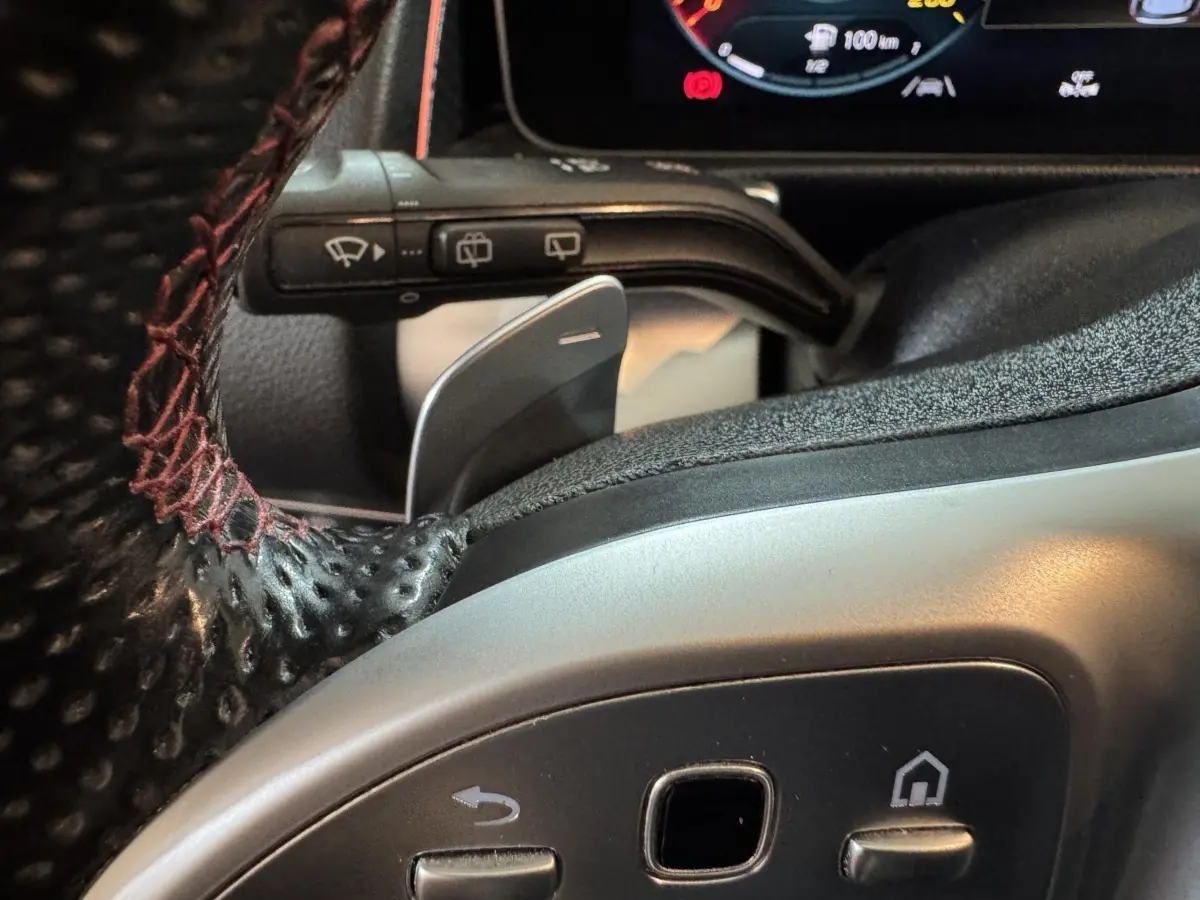 Gros plan sur le volant cuir noir avec surpiqûres rouges du Mercedes GLB 200 d AMG Line, affichage digital en arrière-plan.