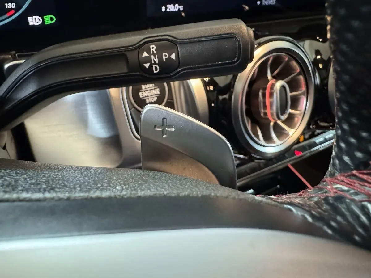 Gros plan sur la commande de boîte automatique et la sortie d'air ronde chromée du tableau de bord d'un Mercedes GLB 200 d noir.