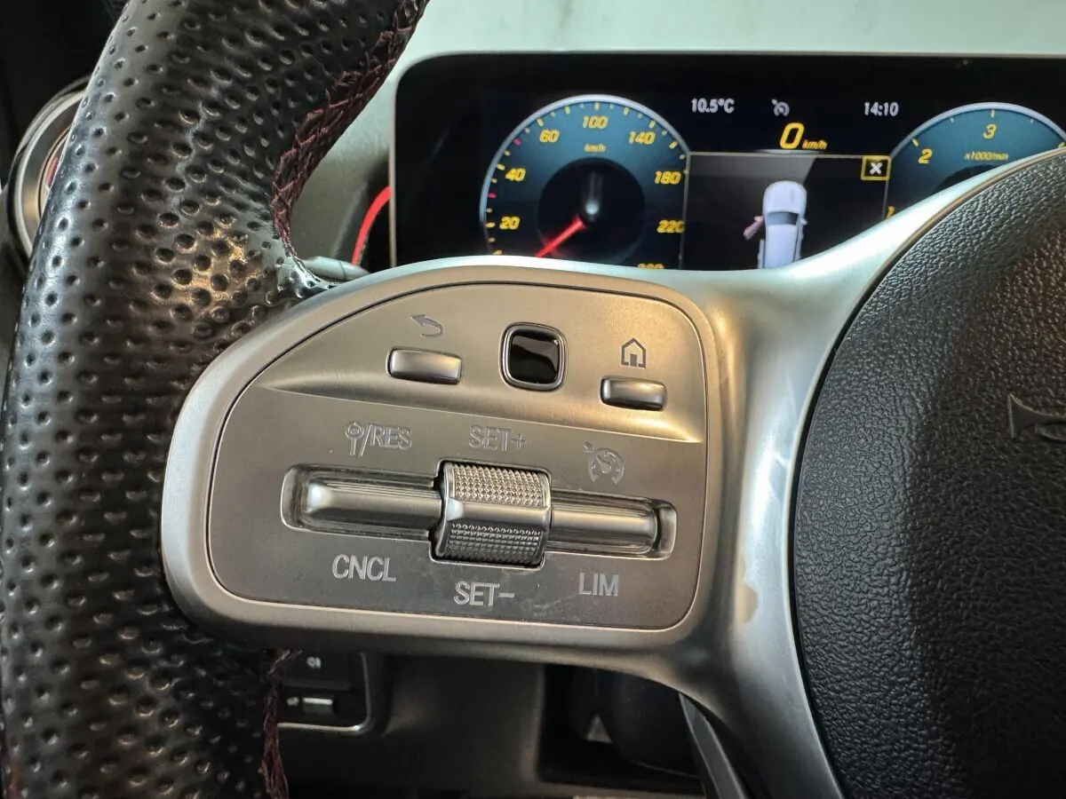 Gros plan sur les commandes du volant cuir perforé du Mercedes GLB 200 d AMG Line noir, avec tableau de bord numérique en arrière-plan.