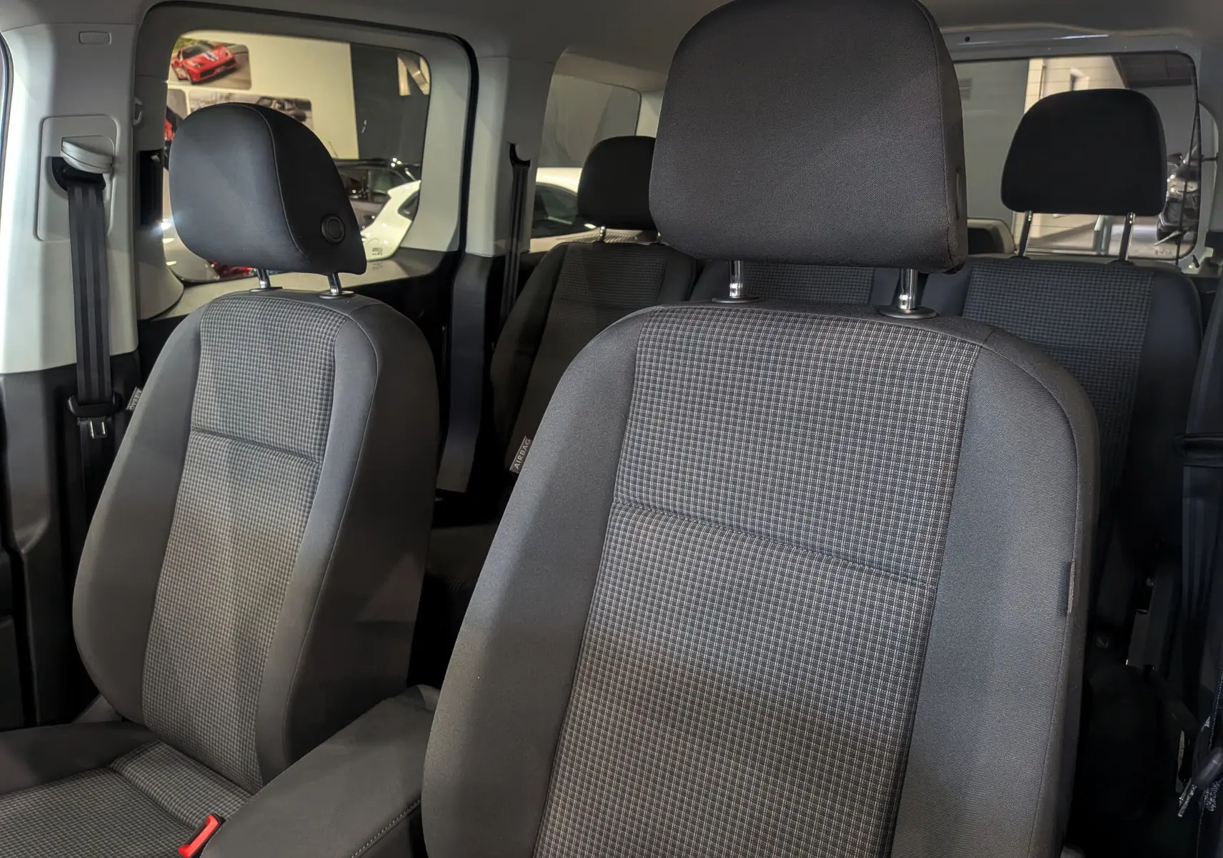 Vue intérieure sur les sièges avant en tissu gris du Volkswagen Caddy 2.0 TDI, avec appuie-têtes et ceinture visible.