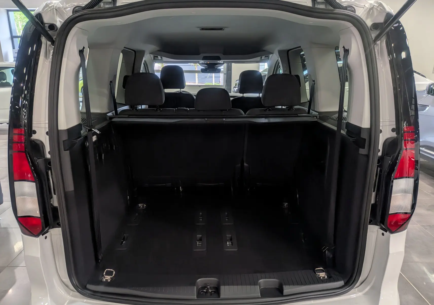 Vue arrière ouverte du coffre spacieux d'un Volkswagen Caddy blanc 2025, montrant les sièges arrière et l'espace de chargement.