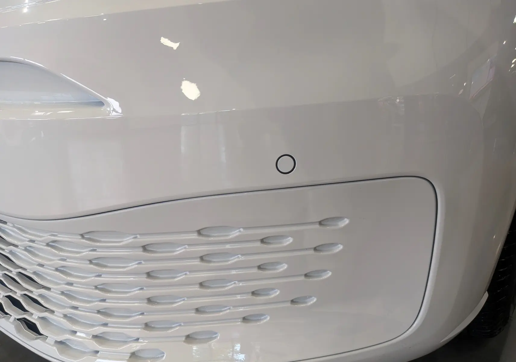 Gros plan sur la partie avant droite blanche du Volkswagen Caddy 2.0 TDI 102 ch avec capteur de stationnement intégré.