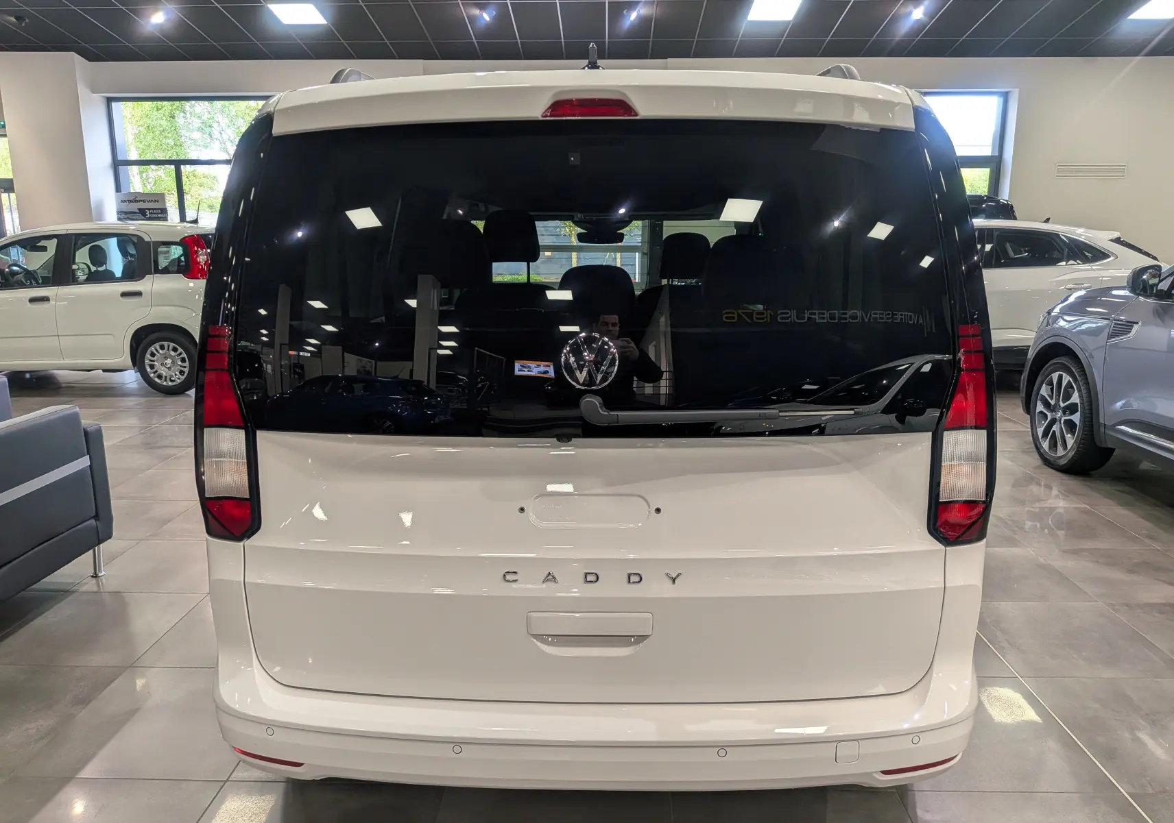 Vue arrière du Volkswagen Caddy blanc 2025 avec vitres arrière teintées et logo VW bien visible en concession.