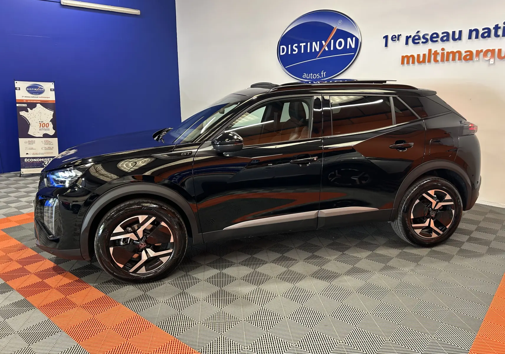 Peugeot 2008 Hybrid 136 GT noir vu de profil droit en intérieur, avec jantes bicolores et toit ouvrant panoramique.