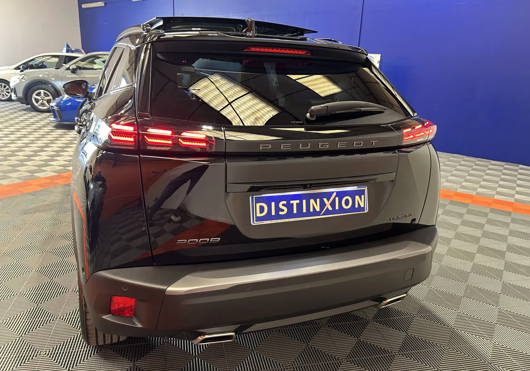 Vue 3/4 arrière d’un Peugeot 2008 Hybrid noir avec feux arrière allumés et toit ouvrant panoramique visible.
