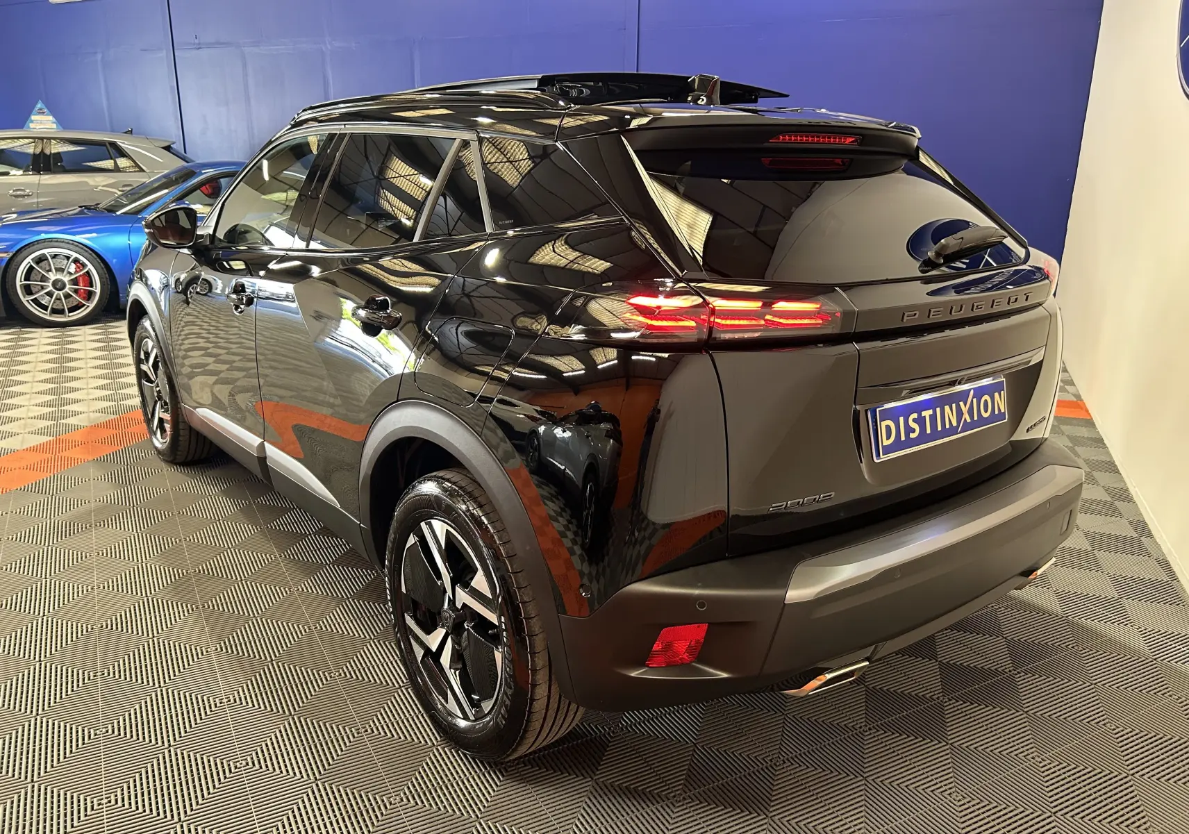 Vue 3/4 arrière droite d’un Peugeot 2008 Hybrid noir brillant avec feux arrière LED et jantes noires en intérieur showroom.
