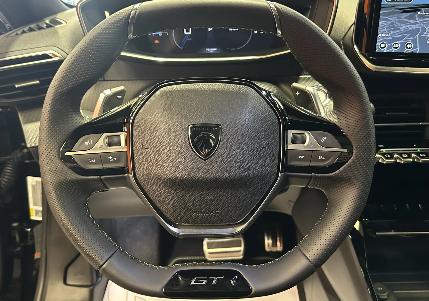 Vue rapprochée du volant noir perforé du Peugeot 2008 Hybrid 136 e-DCS6 GT avec logo lion et badge GT visible.
