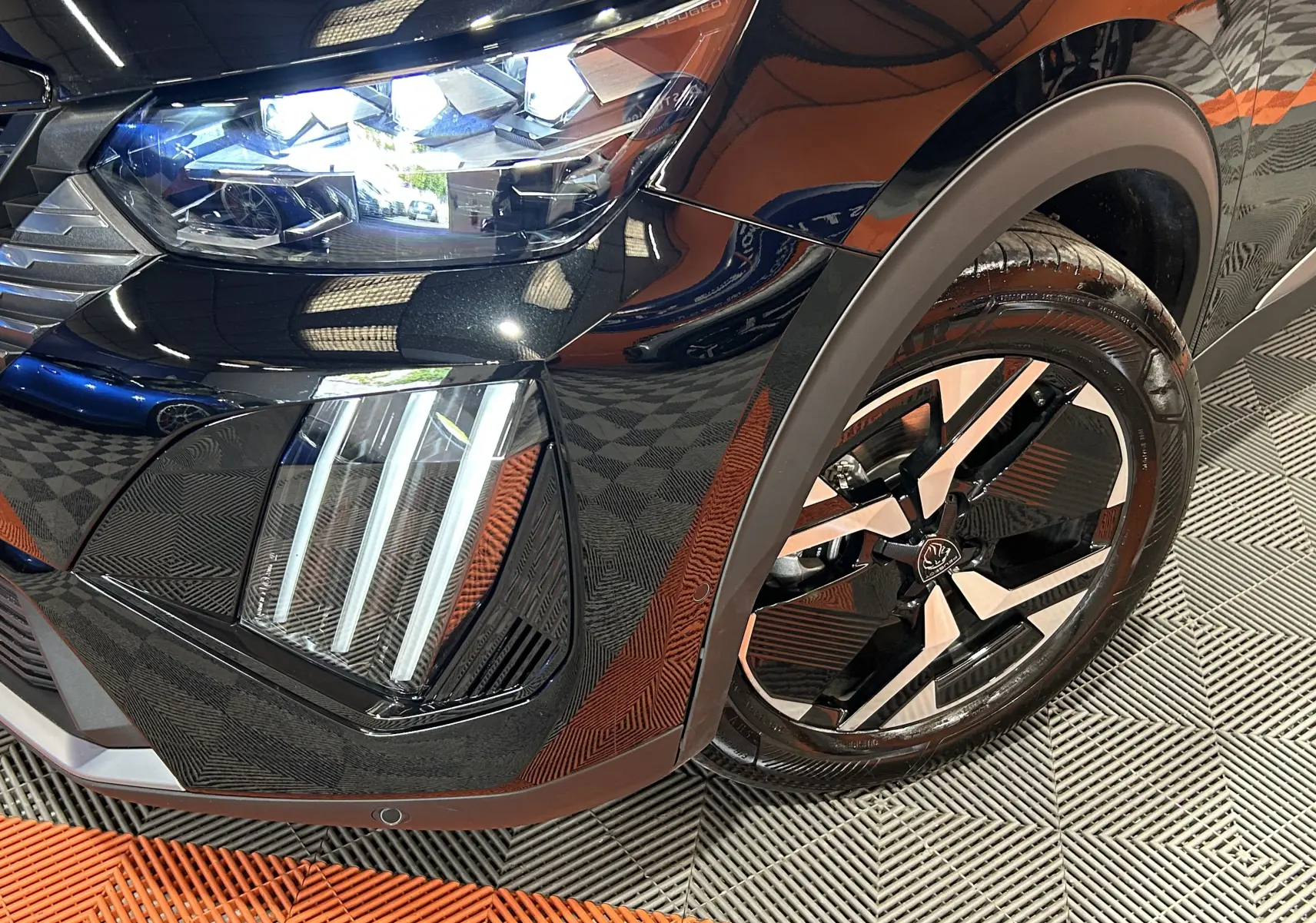 Gros plan sur l’avant droit noir brillant du Peugeot 2008 Hybrid 136 e-DCS6 GT avec ses phares LED et jante alliage bicolore.