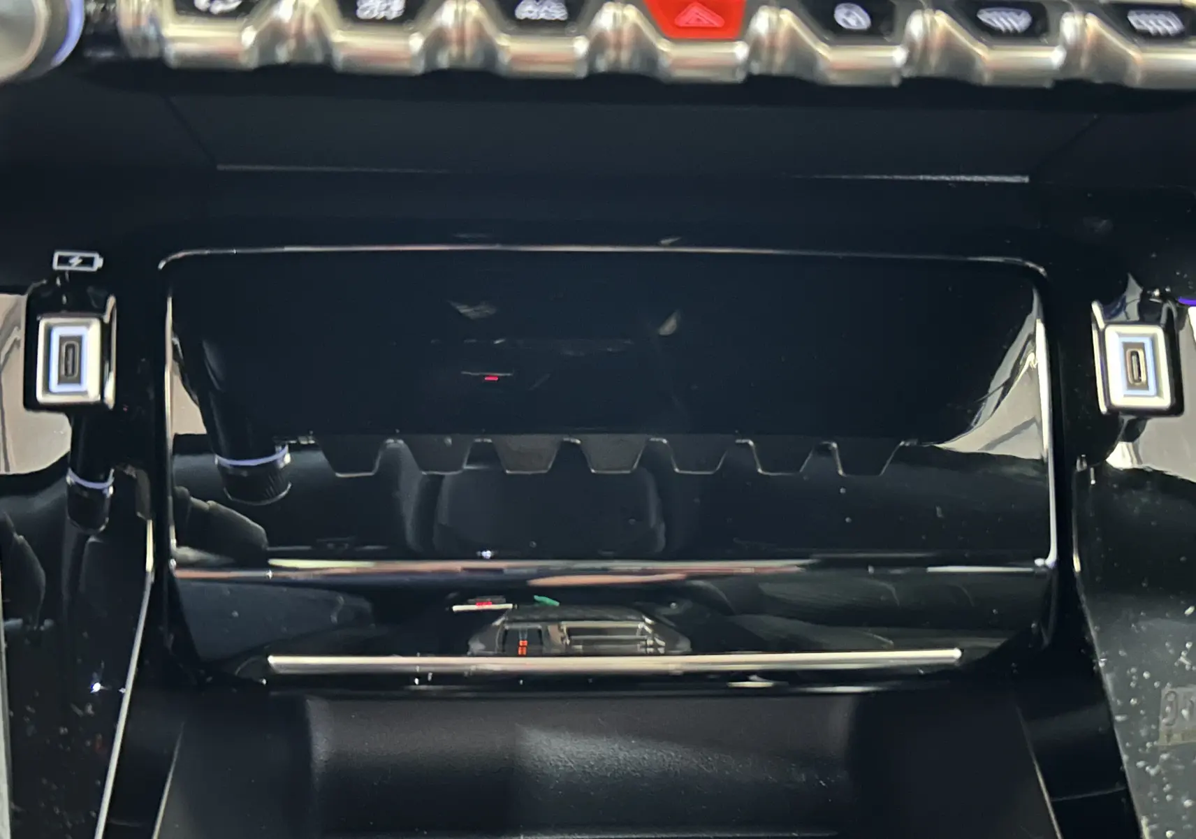 Gros plan sur la console centrale noire brillante du Peugeot 2008 Hybrid 136 e-DCS6 GT avec boutons et ports USB visibles.