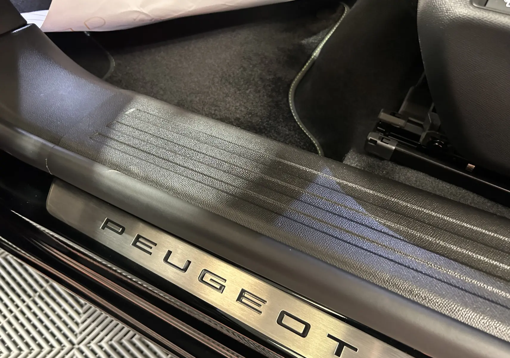 Gros plan sur la plaque de seuil de porte en métal avec logo Peugeot, intérieur noir du SUV 2008 Hybrid 2025.