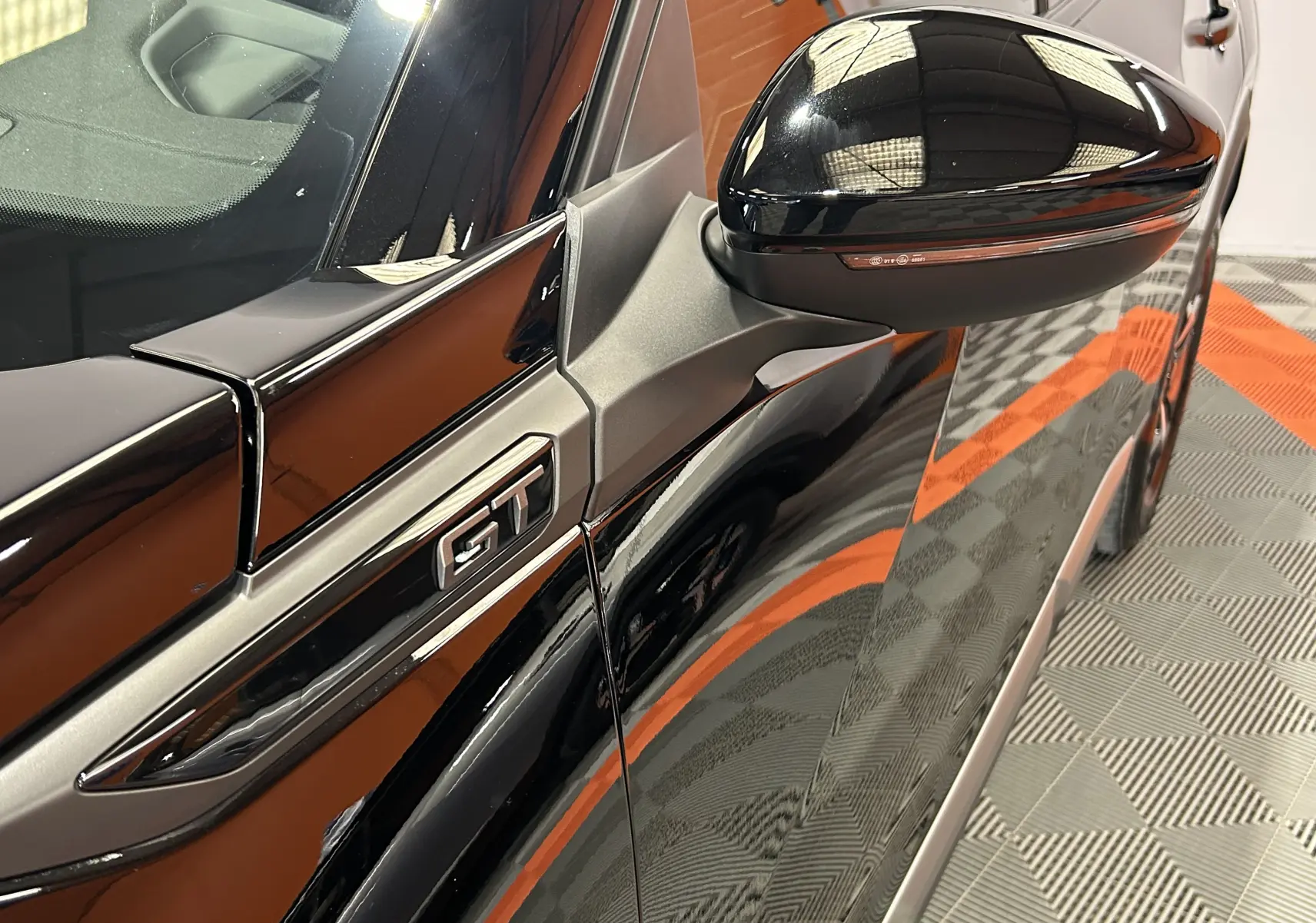 Gros plan sur le rétroviseur et l’inscription GT côté gauche d’un Peugeot 2008 Hybrid noir brillant.