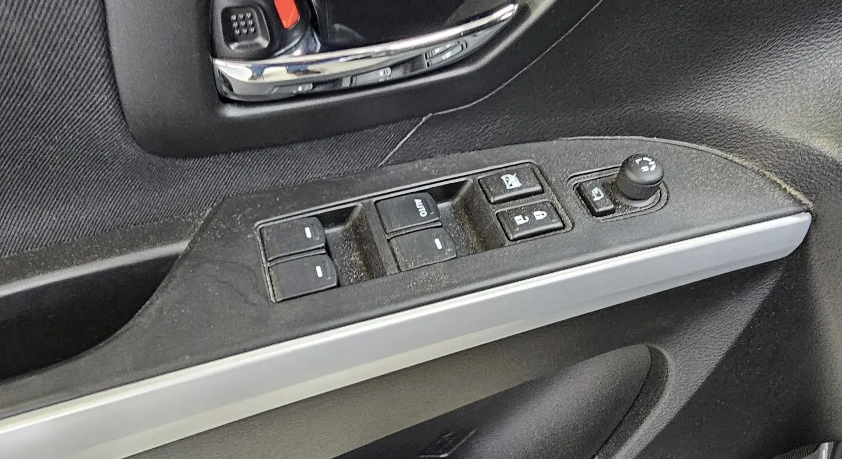 Gros plan sur la commande des vitres électriques et réglage des rétroviseurs côté conducteur d'une Suzuki SX4 S-Cross 2020 noire.