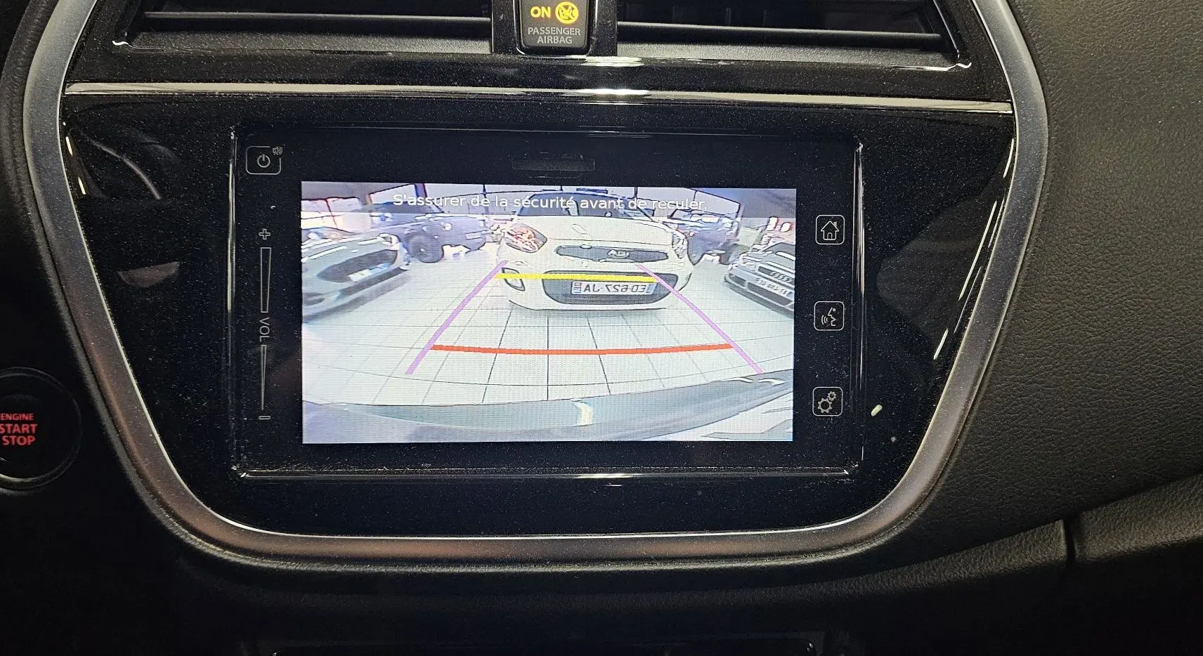 Écran central affichant la caméra de recul du Suzuki SX4 S-Cross 2020 avec vue arrière sur un véhicule blanc en intérieur.