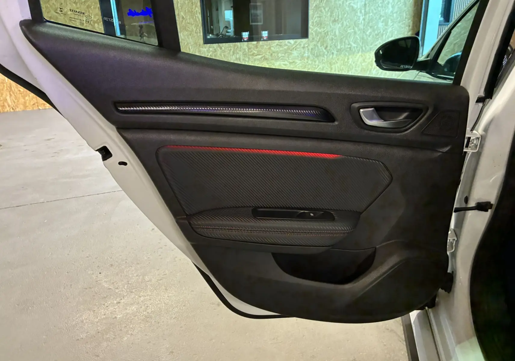 Vue intérieure côté gauche de la porte avant blanche d'une Renault Mégane IV RS 280 avec insert carbone et surpiqûre rouge.