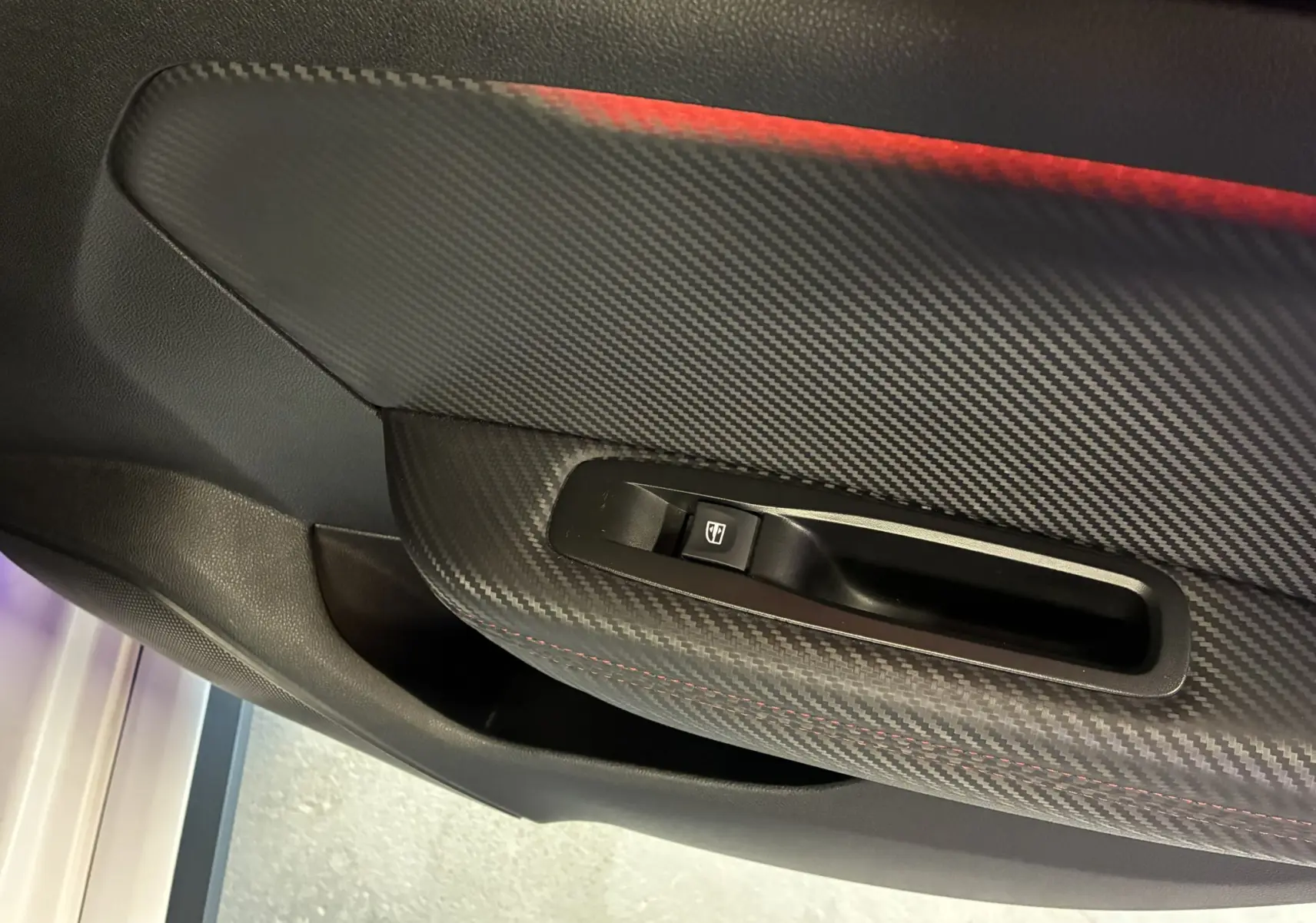 Détail de la commande de lève-vitre côté gauche avec finition carbone et surpiqûres rouges dans une Renault Mégane IV RS 280 blanche.