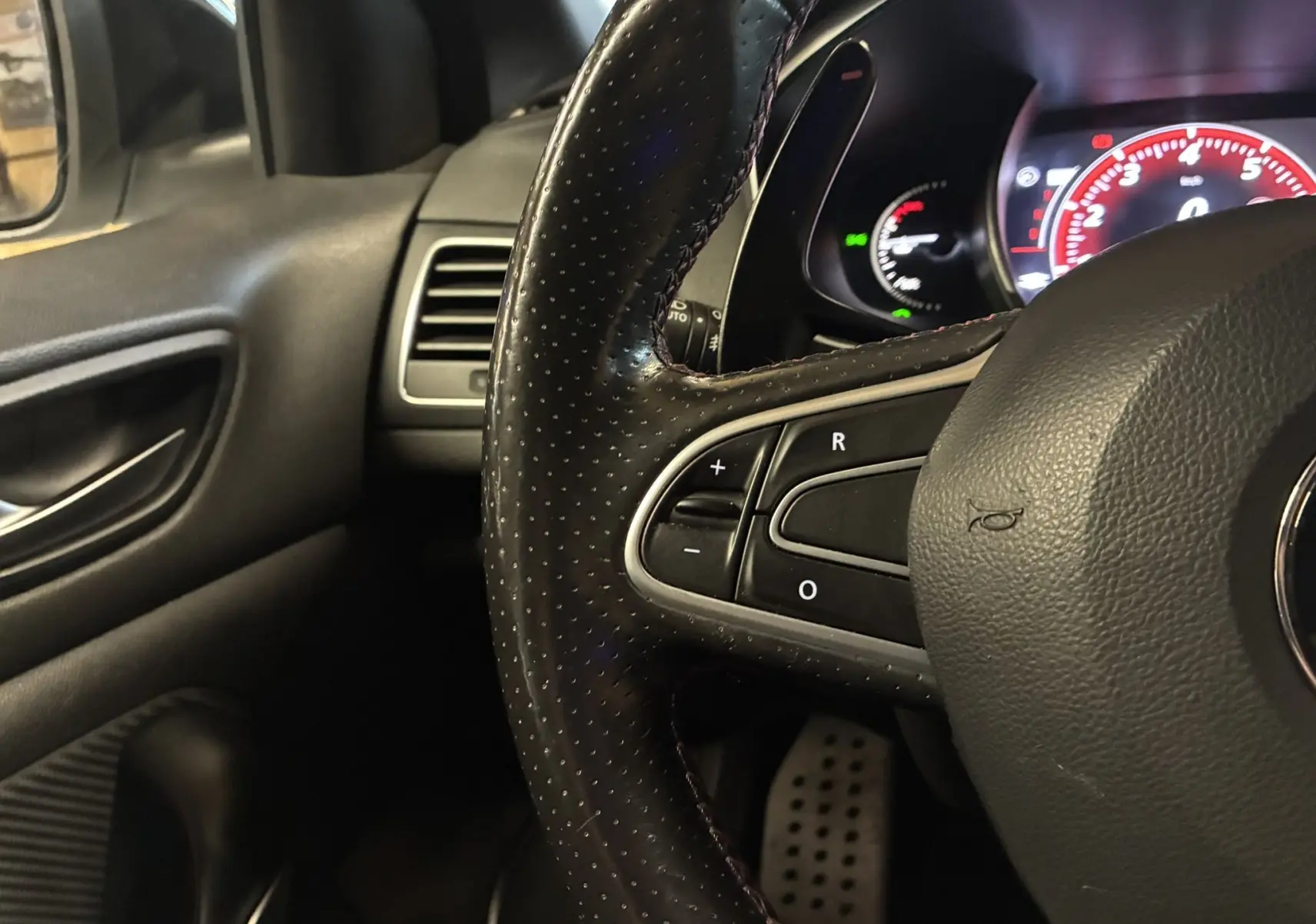 Vue intérieure côté gauche de la Renault Mégane IV RS 280 EDC6 avec sièges sport noirs et surpiqûres rouges, tableau de bord moderne.