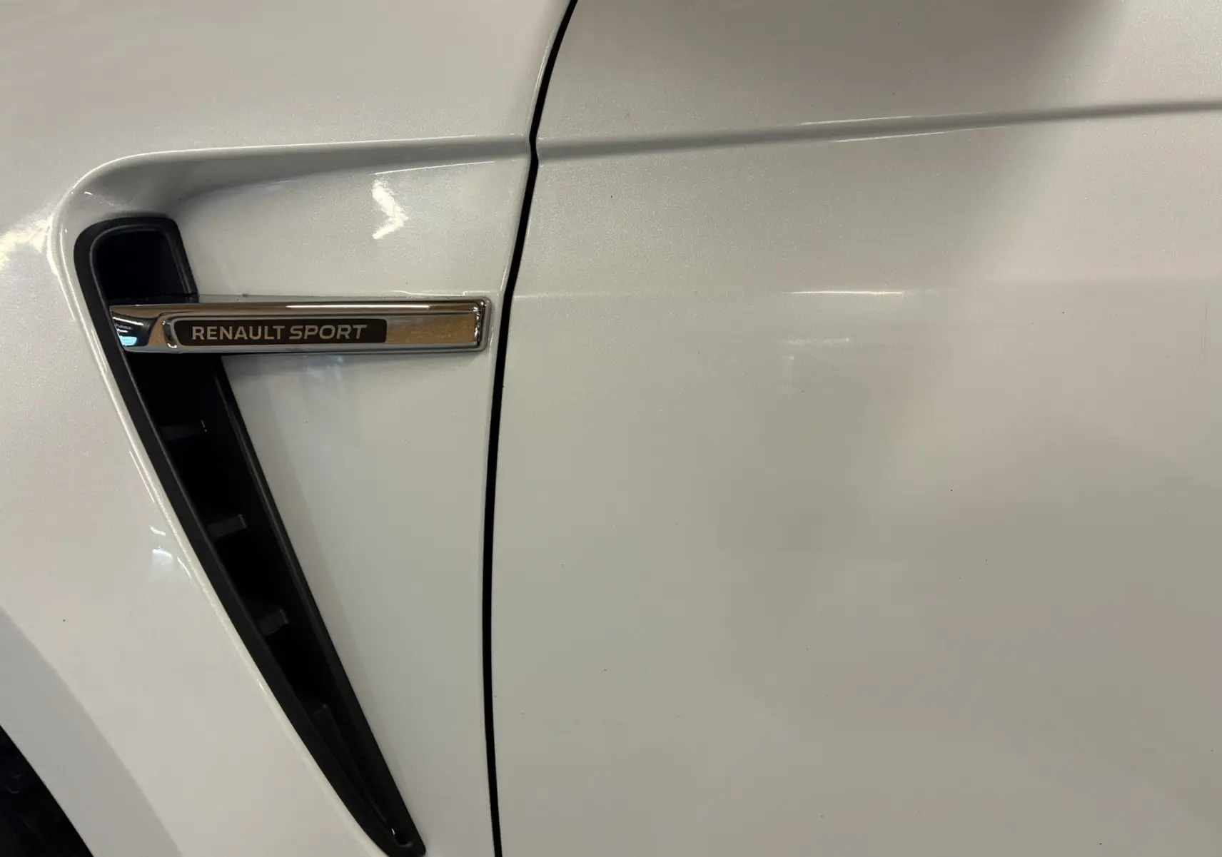 Gros plan sur la prise d'air latérale gauche blanche de la Renault Mégane IV RS 280 EDC6 avec logo Renault Sport chromé.