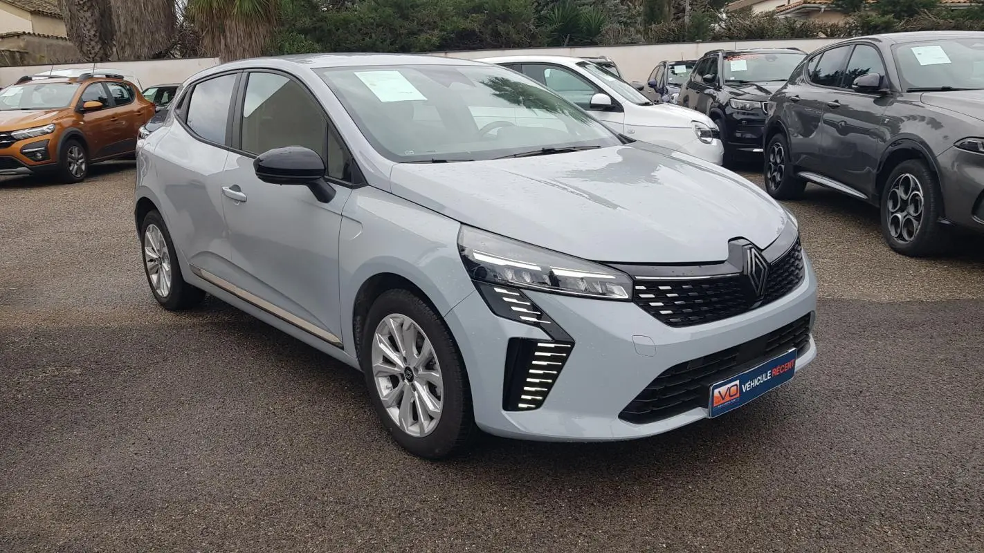 Renault Clio gris vue 3/4 avant droit, avec feux LED distinctifs et calandre noire ajourée.