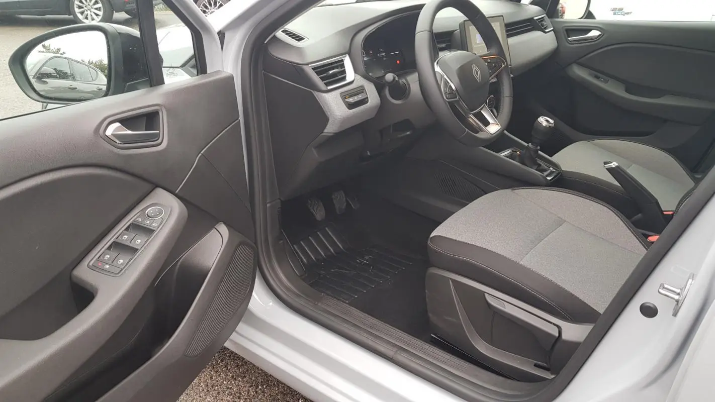 Vue intérieure côté conducteur de la Renault Clio gris 2025, montrant le volant, levier de vitesse manuel et commandes de porte.