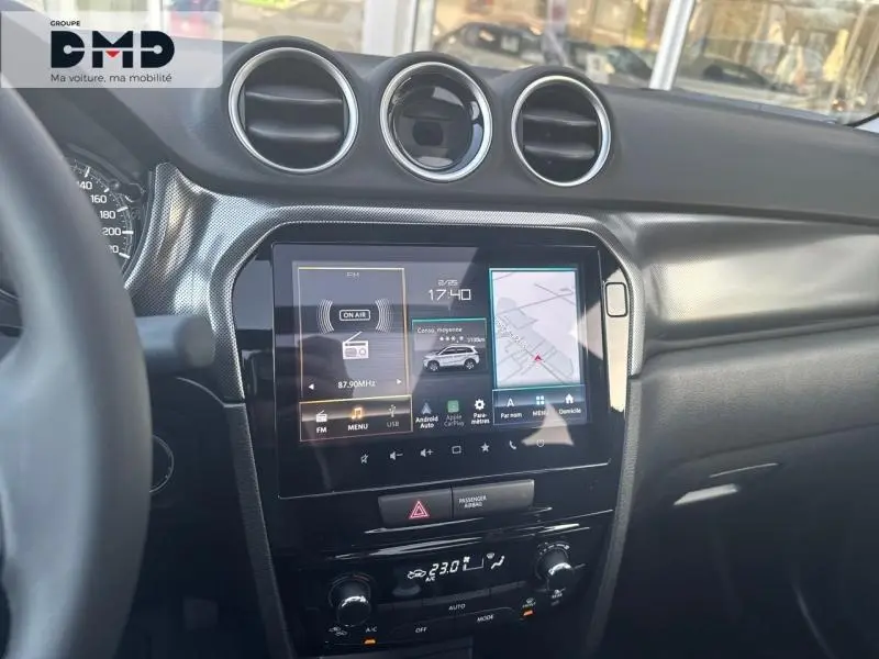 Vue intérieure du tableau de bord du Suzuki Vitara bleu, avec écran tactile et aérateurs ronds chromés.