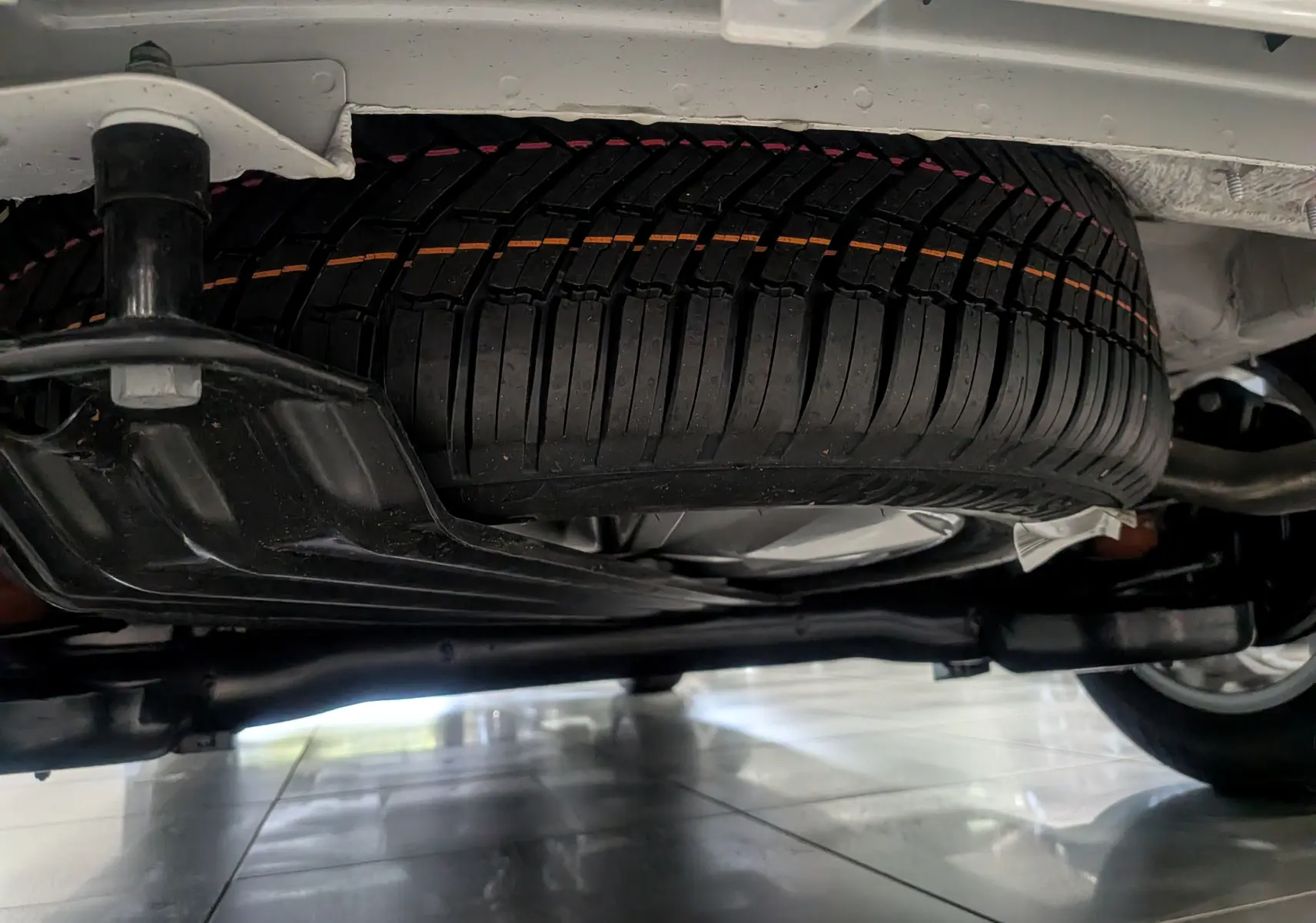 Gros plan sous le Volkswagen Caddy blanc 2025 montrant la roue de secours neuve et la suspension arrière.