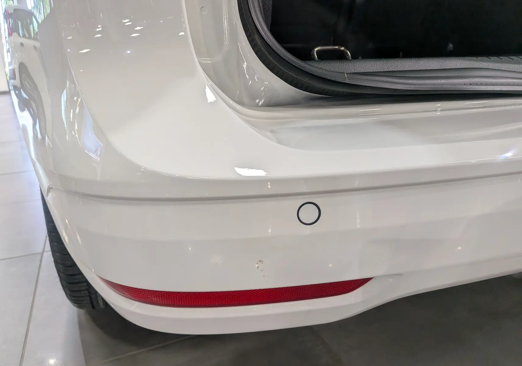 Gros plan sur le pare-chocs arrière blanc du Volkswagen Caddy 2025 avec capteur de recul et feu rouge intégré.