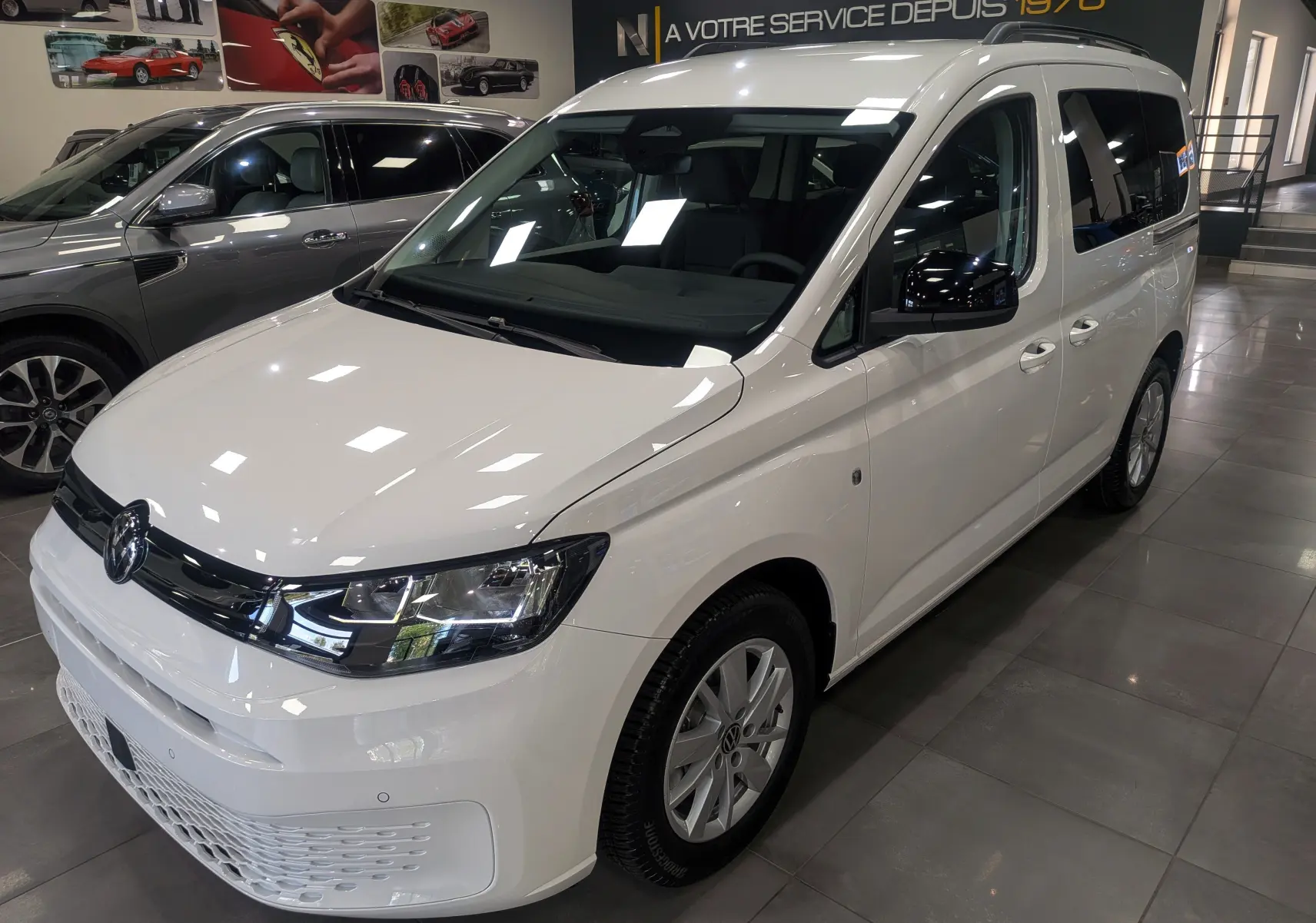 Vue 3/4 avant droite d'un Volkswagen Caddy blanc 2025 en showroom, avec calandre noire et jantes argentées.