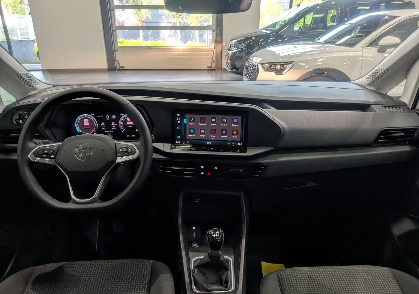 Vue intérieure avant du Volkswagen Caddy blanc 2025, mettant en valeur le volant multifonction et l’écran tactile central.