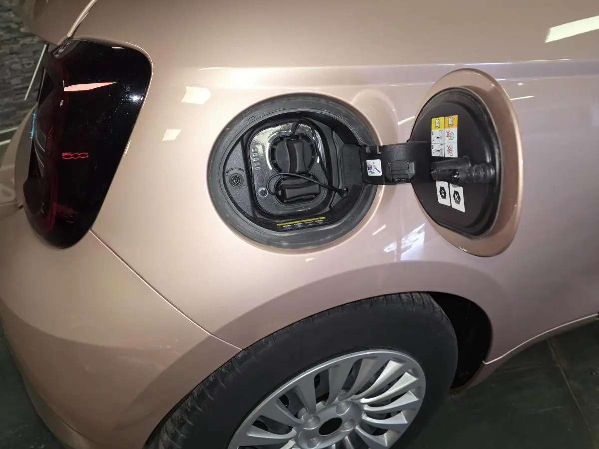 Vue arrière gauche d'une FIAT 500 Cabriolet électrique rose métallisée avec feu arrière LED et capote noire.
