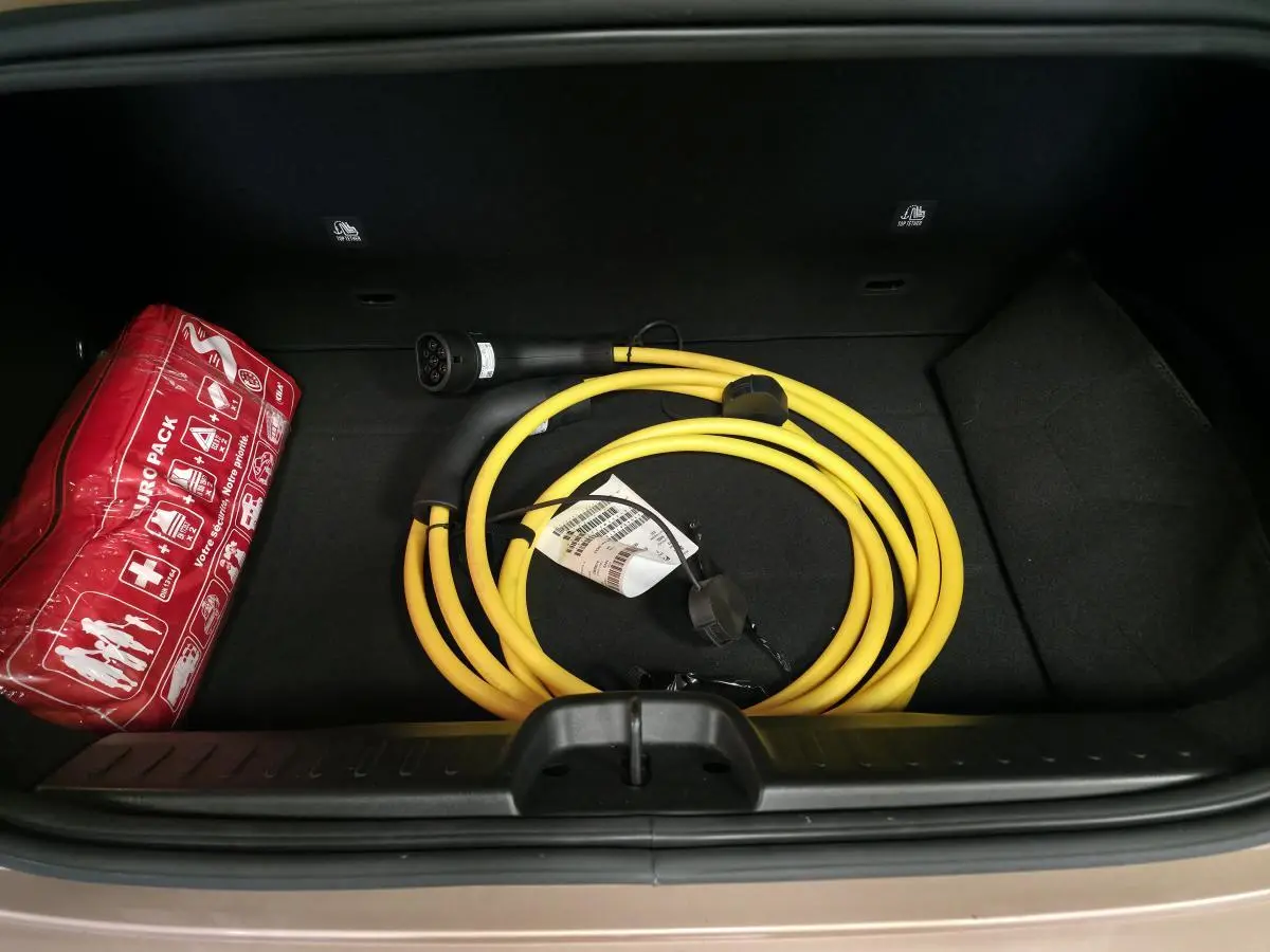 Vue plongeante sur le coffre d'une FIAT 500 Cabriolet électrique rose, avec câble de recharge jaune et trousse de secours rouge.