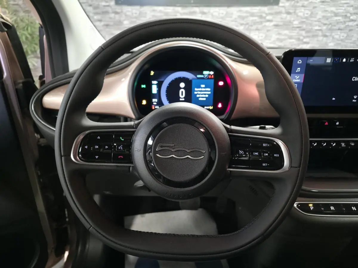 Vue centrée du volant noir Soft-Touch de la Fiat 500 Cabriolet électrique 2023 avec tableau de bord rose métallisé.