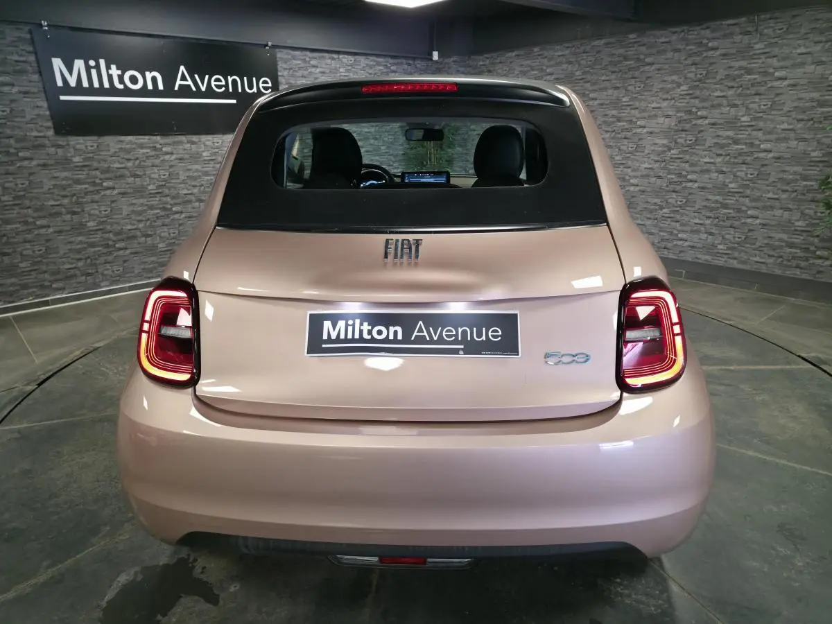Vue arrière d'une FIAT 500 Cabriolet électrique rose métallisée avec capote noire et feux arrière LED allumés.