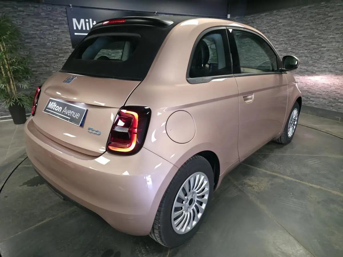 Vue 3/4 arrière droite d'une FIAT 500 Cabriolet électrique rose métallisé avec capote noire et feux LED distinctifs.