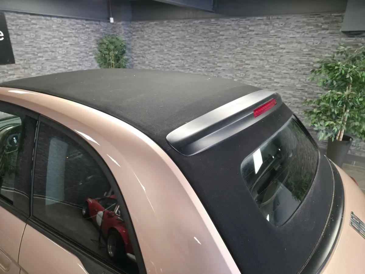 Vue arrière 3/4 d'une FIAT 500 Cabriolet électrique rose avec capote noire et feu stop intégré sur le toit.