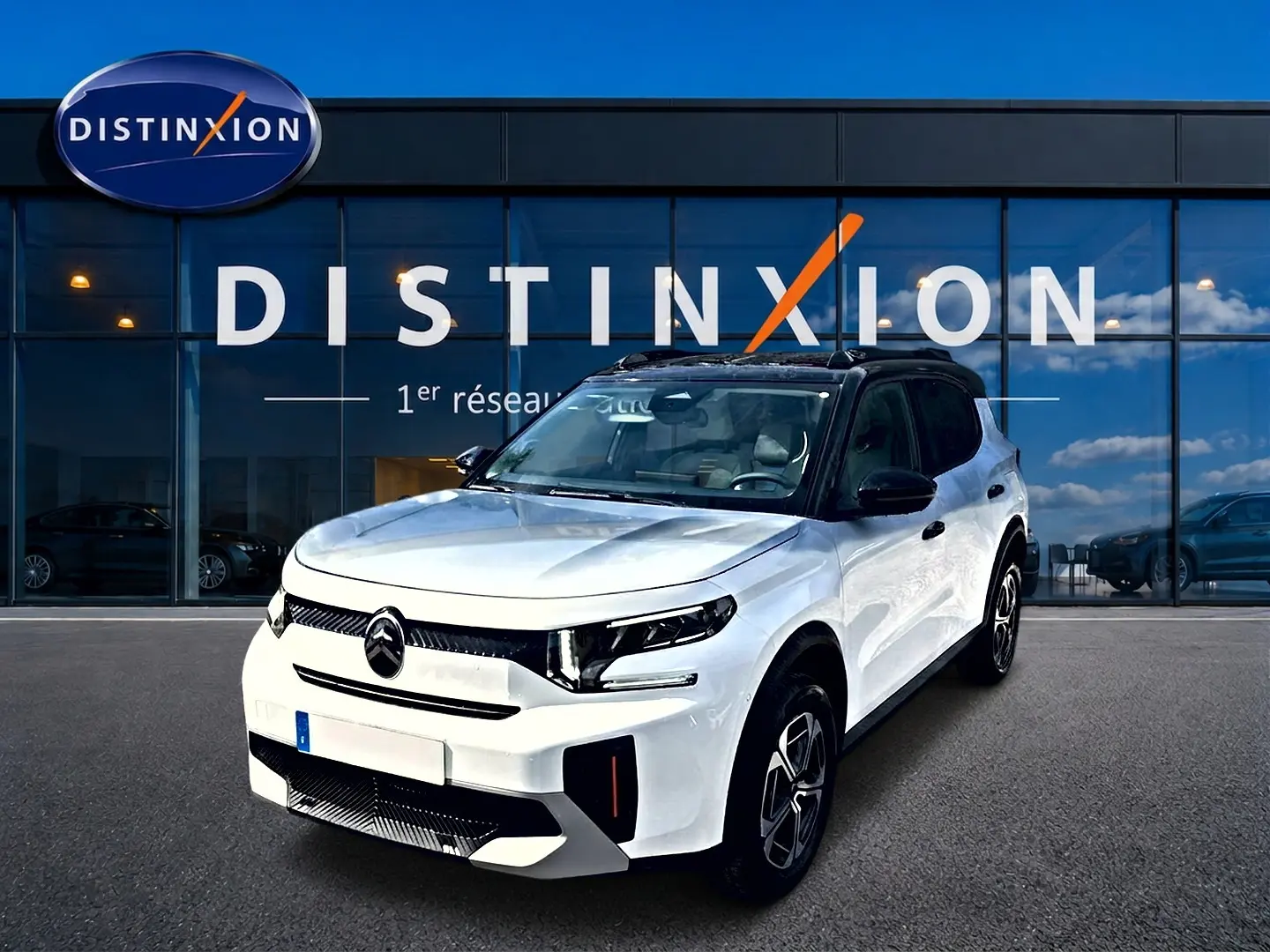 Vue 3/4 avant droite d'une Citroën C3 Aircross blanche avec toit noir et jantes alu devant un showroom Distinxion.