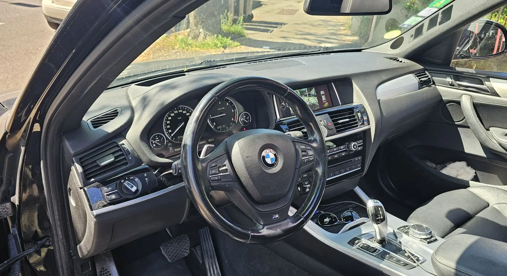Vue intérieure côté conducteur d'un BMW X4 xDrive20dA noir, avec volant multifonction et tableau de bord moderne.