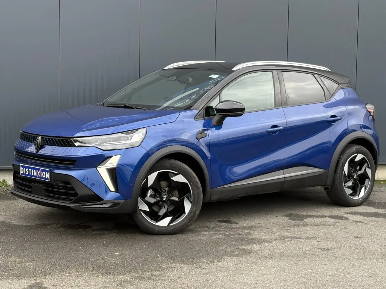 Renault Captur 2025 bleu Iron et noir, vue 3/4 avant droit, avec jantes alu noires diamantées et railing de toit alu.