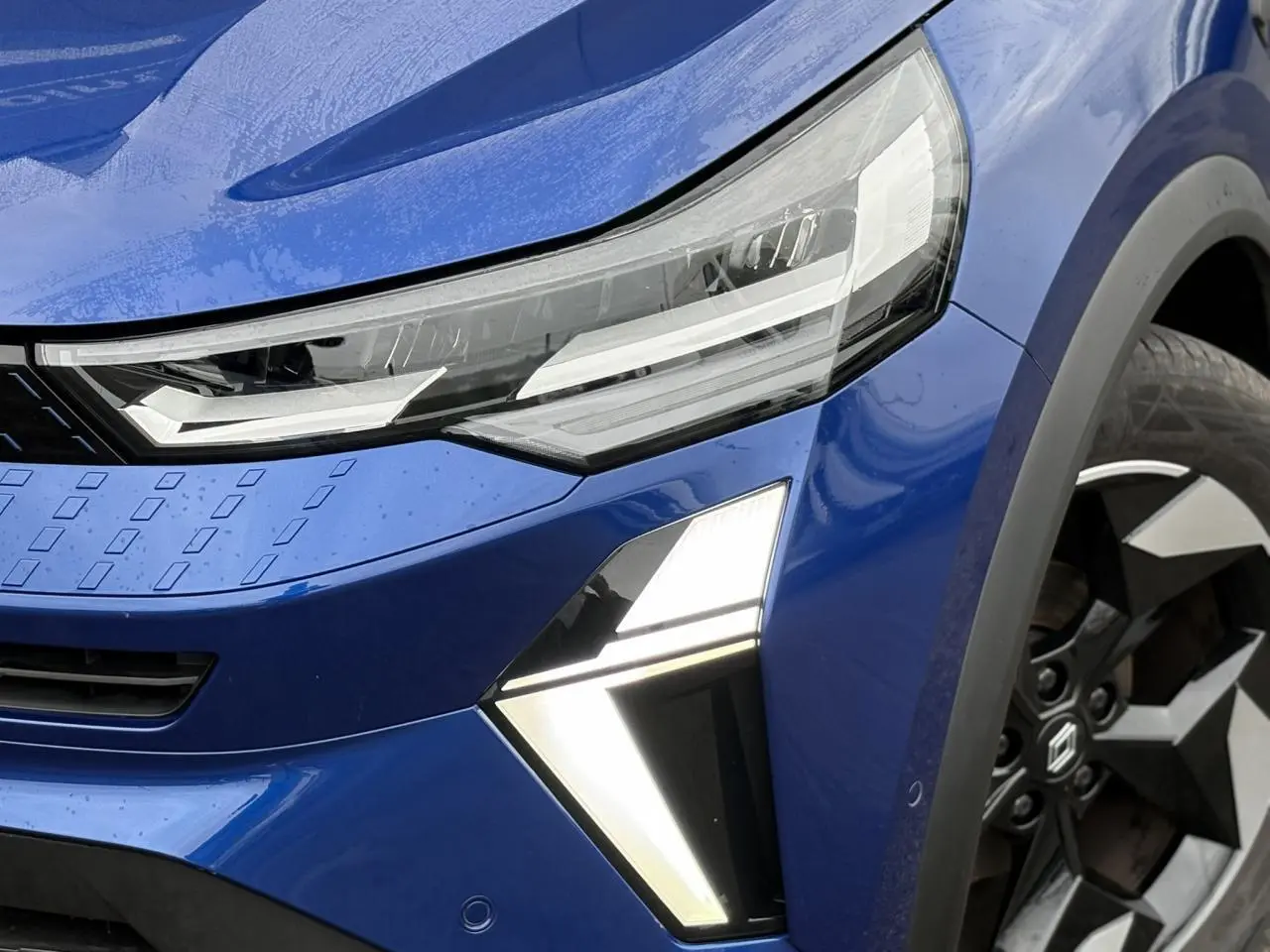 Gros plan sur l'avant droit du Renault Captur bleu Iron, mettant en valeur les phares LED et la jante alu diamantée noire.