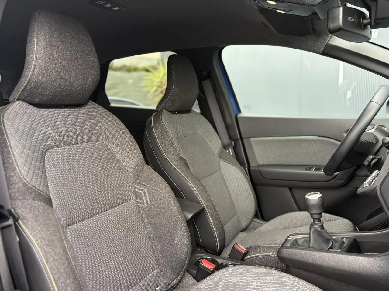 Vue intérieure côté droit du Renault Captur 2025, sièges tissu gris avec surpiqûres jaunes et levier de vitesse manuel.