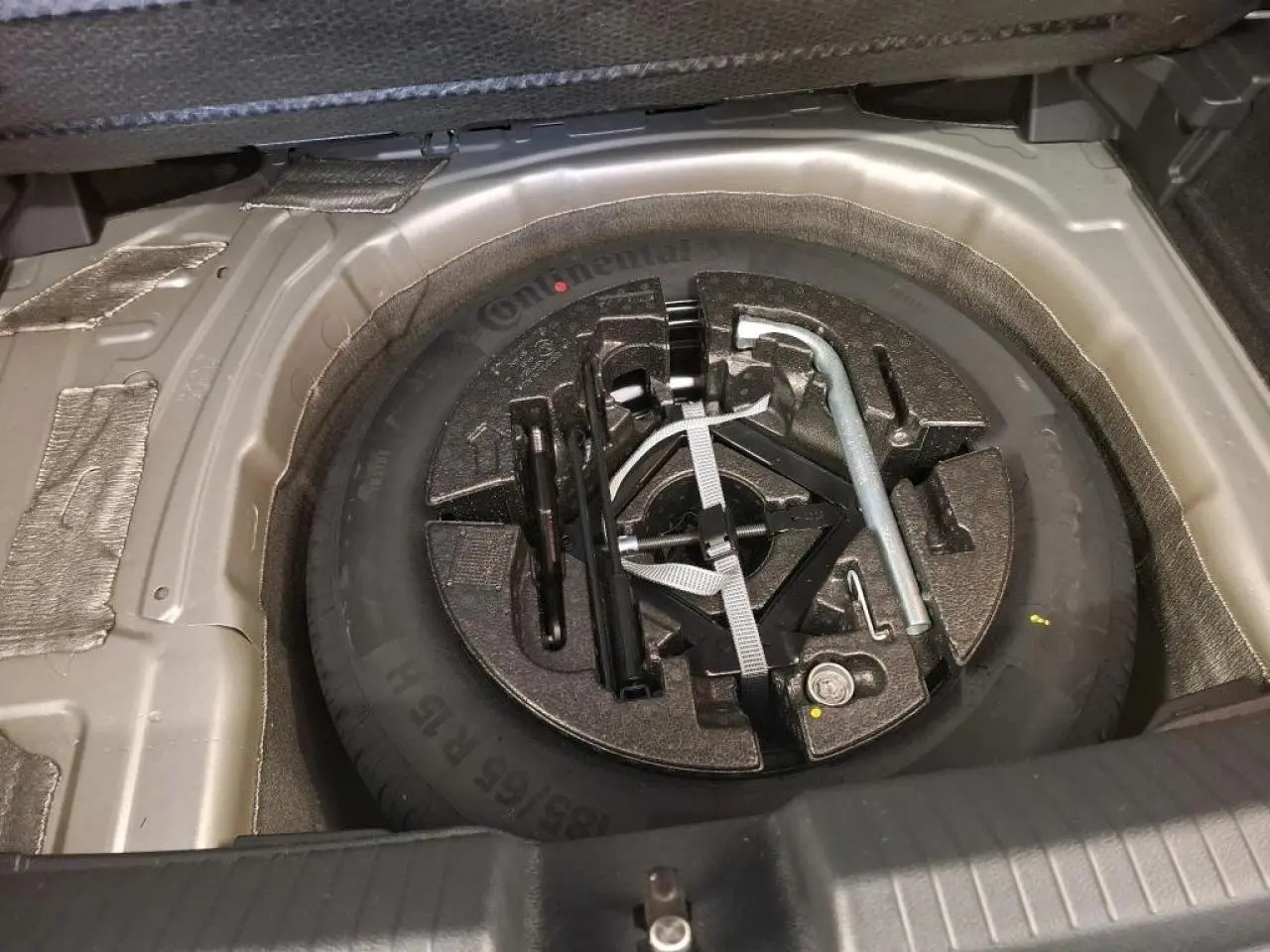 Gros plan sur la roue de secours acier 15 pouces et outillage de bord dans le coffre d’une Volkswagen Polo gris clair.