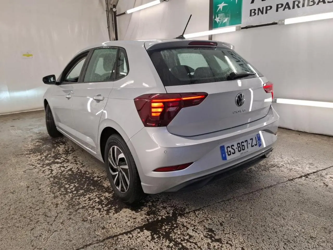 Vue 3/4 arrière droit d'une Volkswagen Polo gris clair avec feux arrière allumés dans un garage.