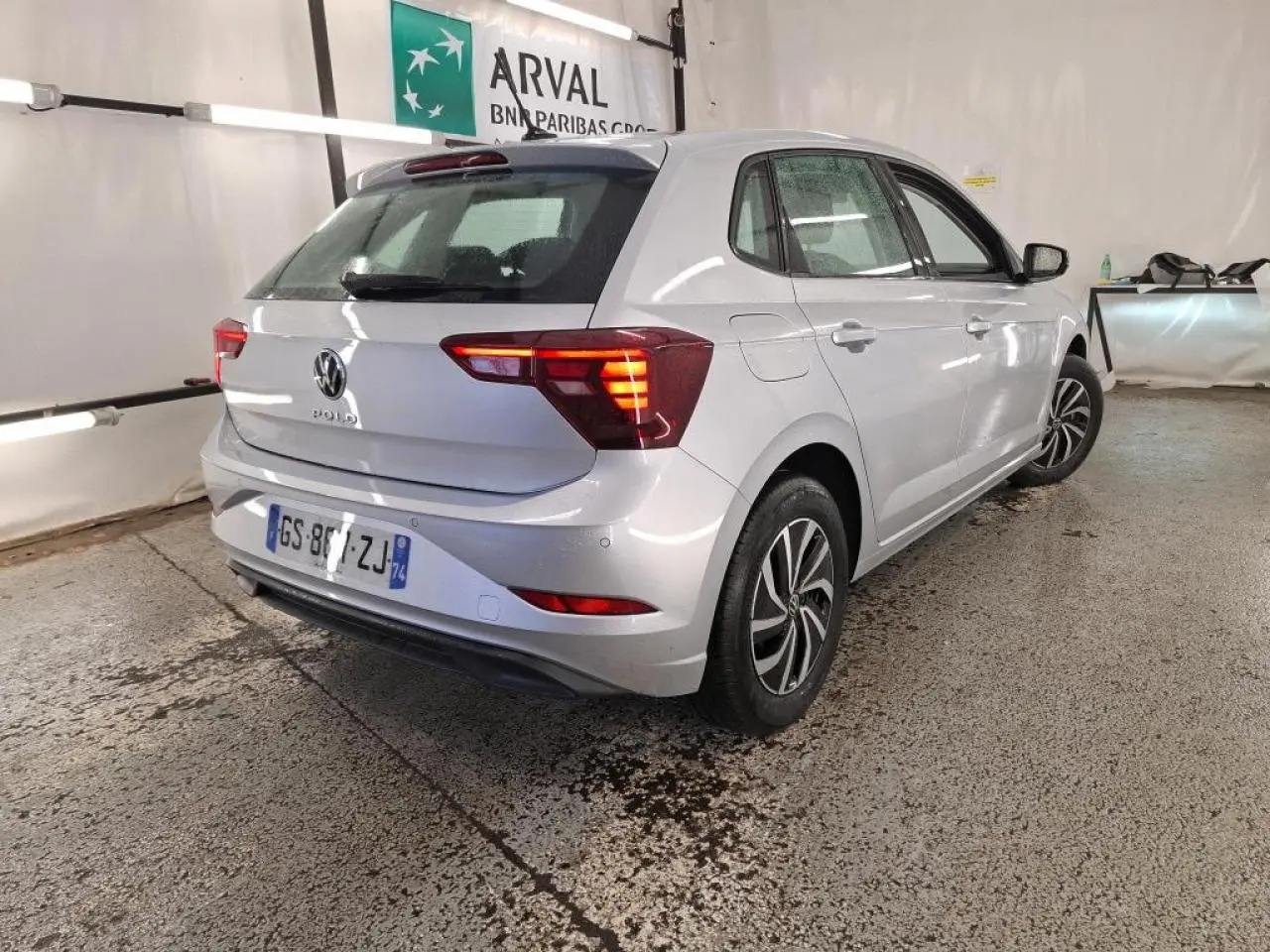 Vue 3/4 arrière droit d'une Volkswagen Polo gris clair avec feux arrière allumés dans un garage.